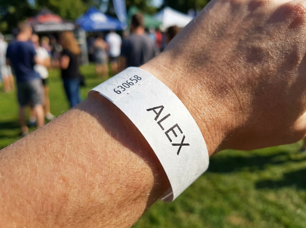 Pulseira Tyvek branca impressa com o primeiro nome de uma crianca e um numero de telefone de emergencia, usada no pulso de uma crianca pequena num evento ao ar livre